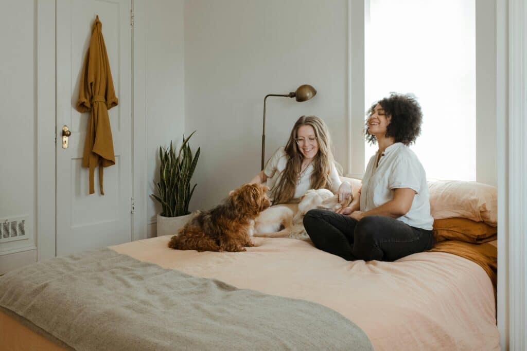 two woman sitting on a bed with a dog