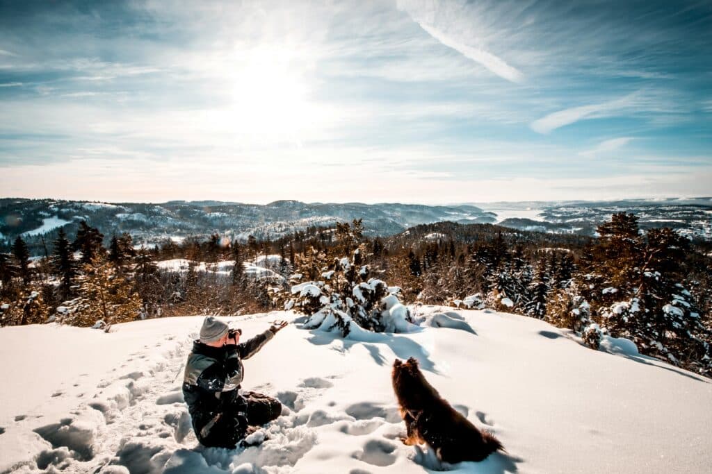 a man and a dog on a mountain in the winter time surrounded by snow